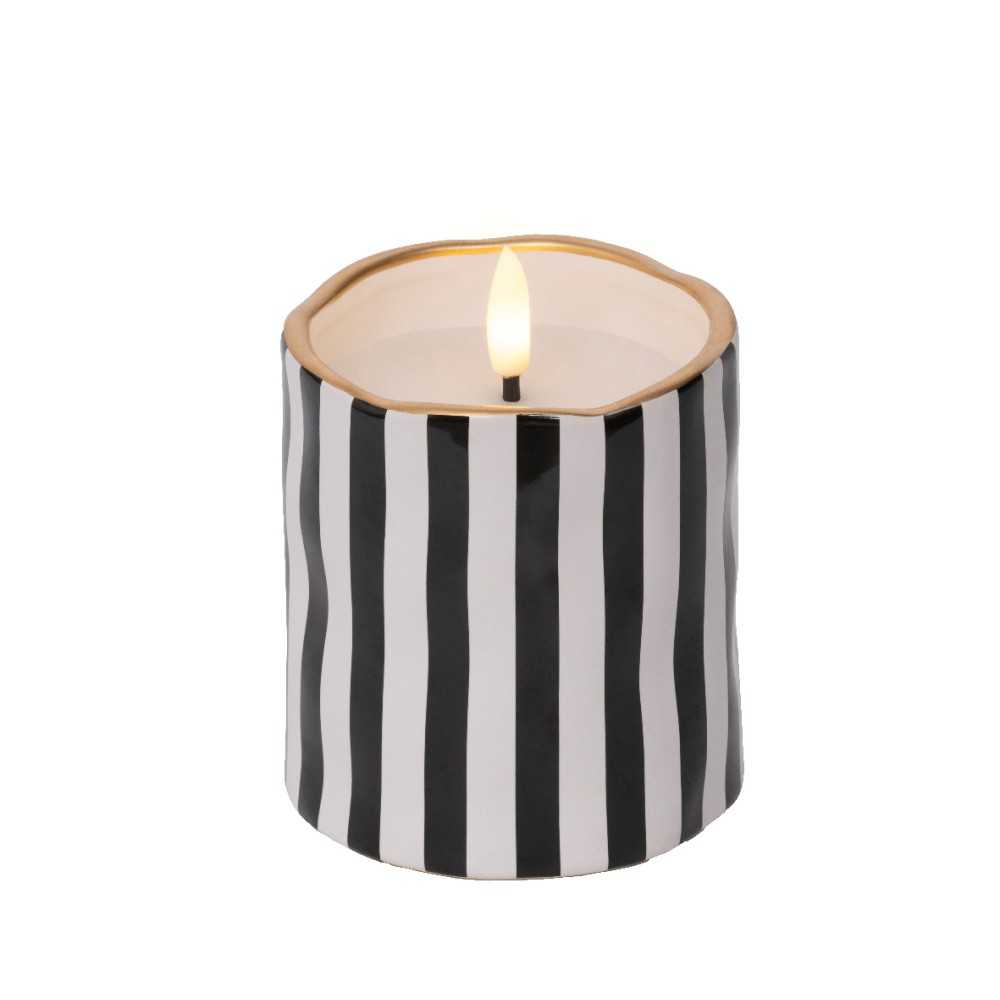 A round candle with black and white stripes and a gold rim, softly glowing from within.