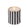 A round candle with black and white stripes and a gold rim, softly glowing from within.