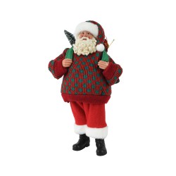 A cheerful Santa in a red and green sweater, holding a small tree and wearing black boots.