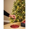 A hand places a thin white stick into a sparkling red base near a softly lit Christmas tree.