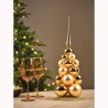 Gouden kerstboom van ballen met een glanzende punt, naast twee elegante glazen.
