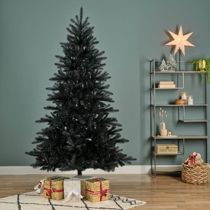 Zwart kunstkerstboom tegen een groene muur, met geschenken onderaan en een ster bovenop.