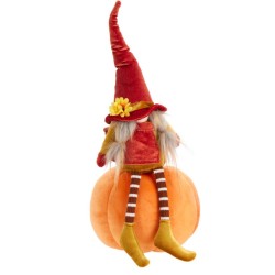 Een schattige pop met een rode hoed zit op een oranje pompoen, met gestreepte sokken.