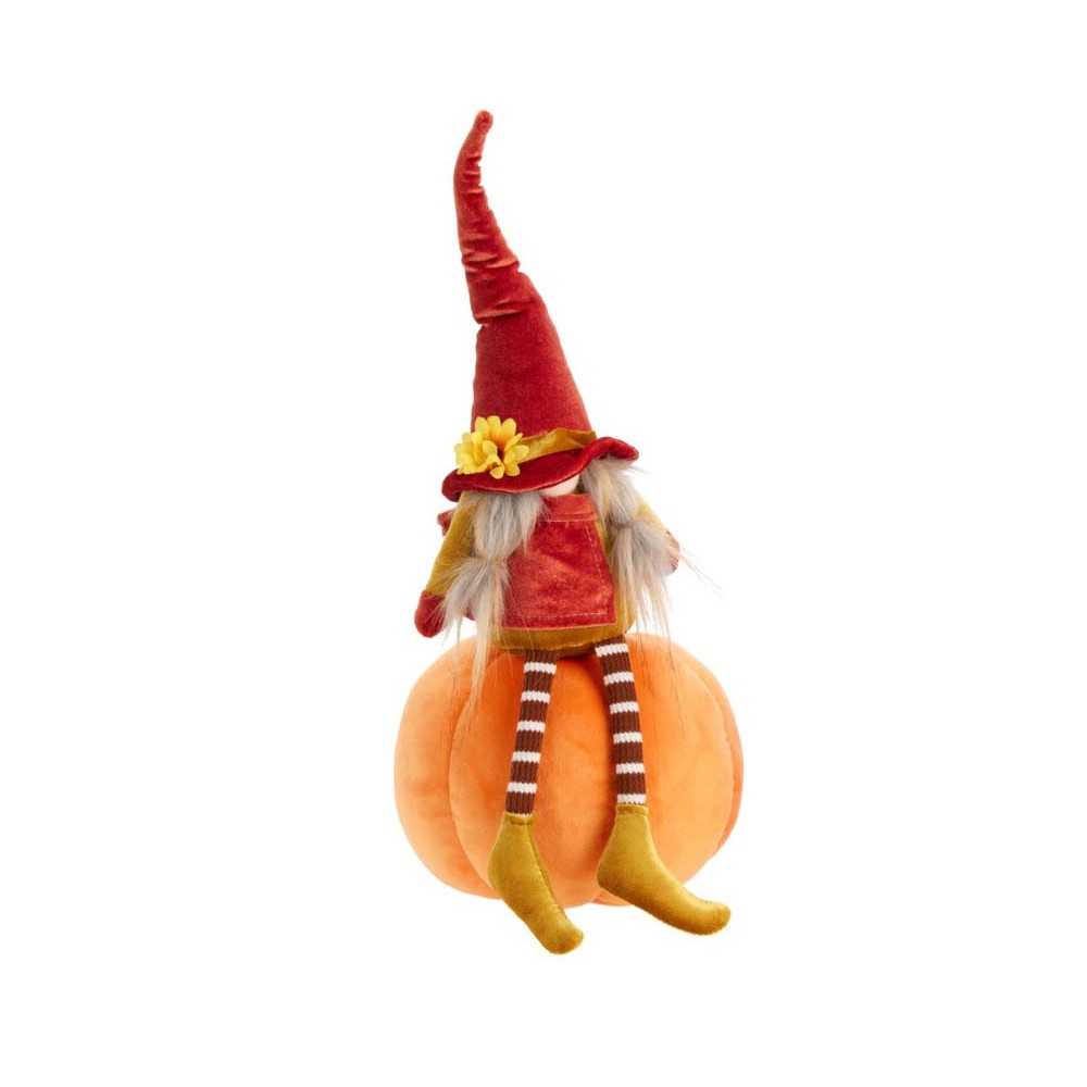 A whimsical doll in a red hat sits on a plush orange pumpkin, with striped stockings.