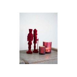 Two red nutcracker figures stand beside a festive candle on a light-colored surface.