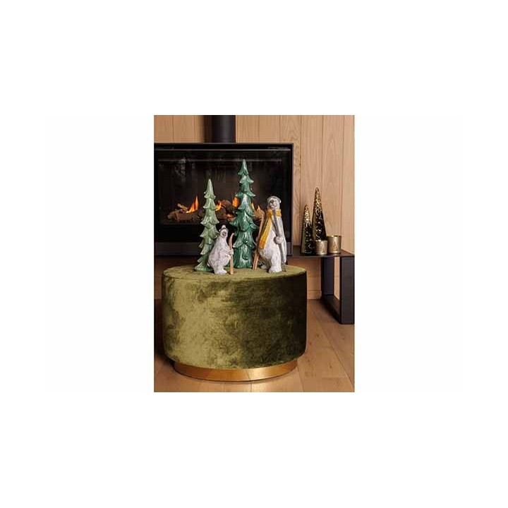 Decoratieve figuren van dieren en bomen op een groene, fluweelachtige poef bij een haard.