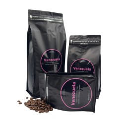 Drie zwarte koffiezakken met roze labels, omringd door losse koffiebonen.