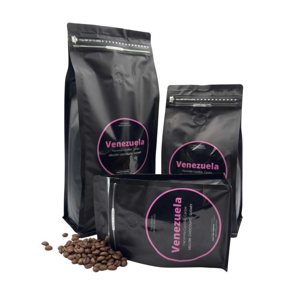 Drie zwarte koffiezakken met roze labels, omringd door losse koffiebonen.