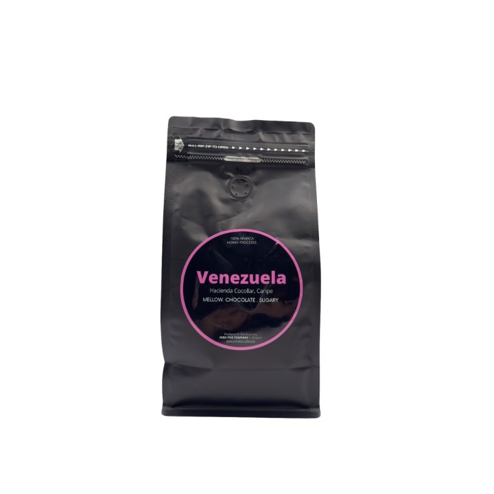 Zwarte pakket met ronde, roze label en tekst over Venezolaanse koffie. Minimalistische stijl.