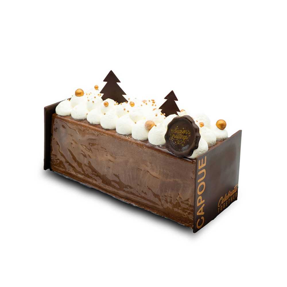 A rich chocolate log cake topped with white cream, golden spheres, and chocolate trees.