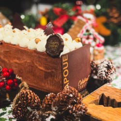 A festive chocolate log cake adorned with cream, chocolate decorations, and holiday accents.
