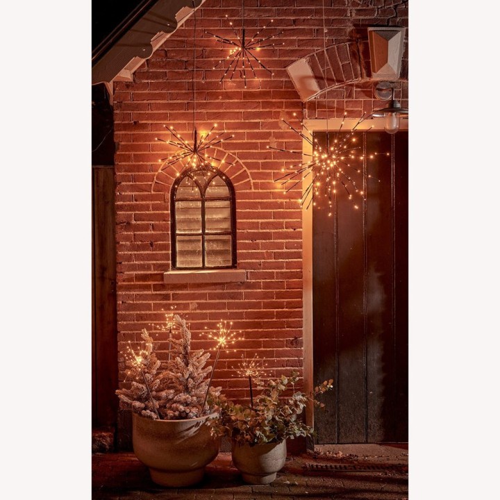 Warmly lit brick wall with decorative stars, potted plants, and a charming arched window.