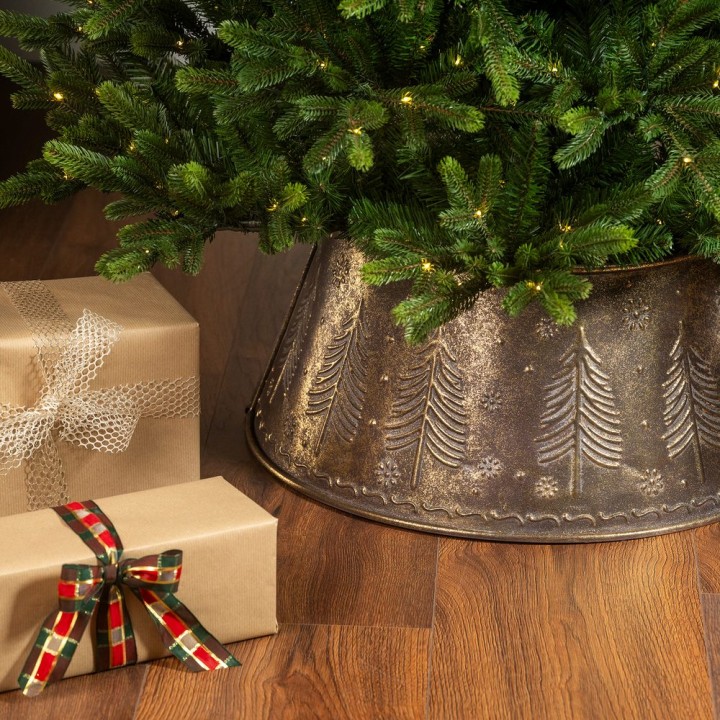 Een groene kerstboom met een metalen voet en cadeaus in kraftpapier met een strik.