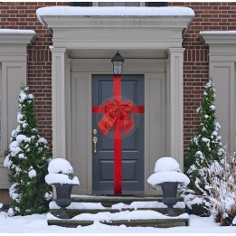 A festive gray door adorned with a large red bow amid snowy greenery.
