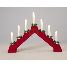 A red wooden candle holder with seven white candles and green accents resembling pine.